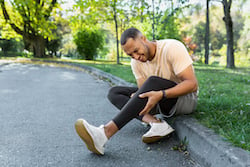 Runner injured his leg while jogging in the park near the trees.